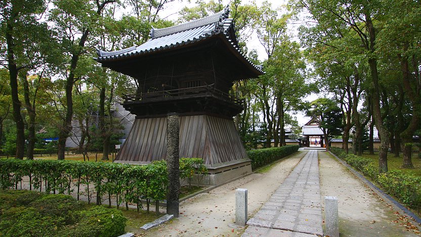 A photo of a path inside the Shofukuji temple grounds. The foliage is very green and well-kept. To the left is a belfry.